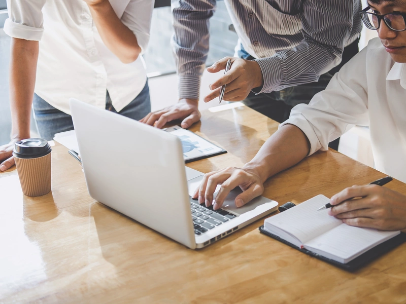 Bild dreier Arbeitskollegen, die an einem Laptop gemeinsam arbeiten