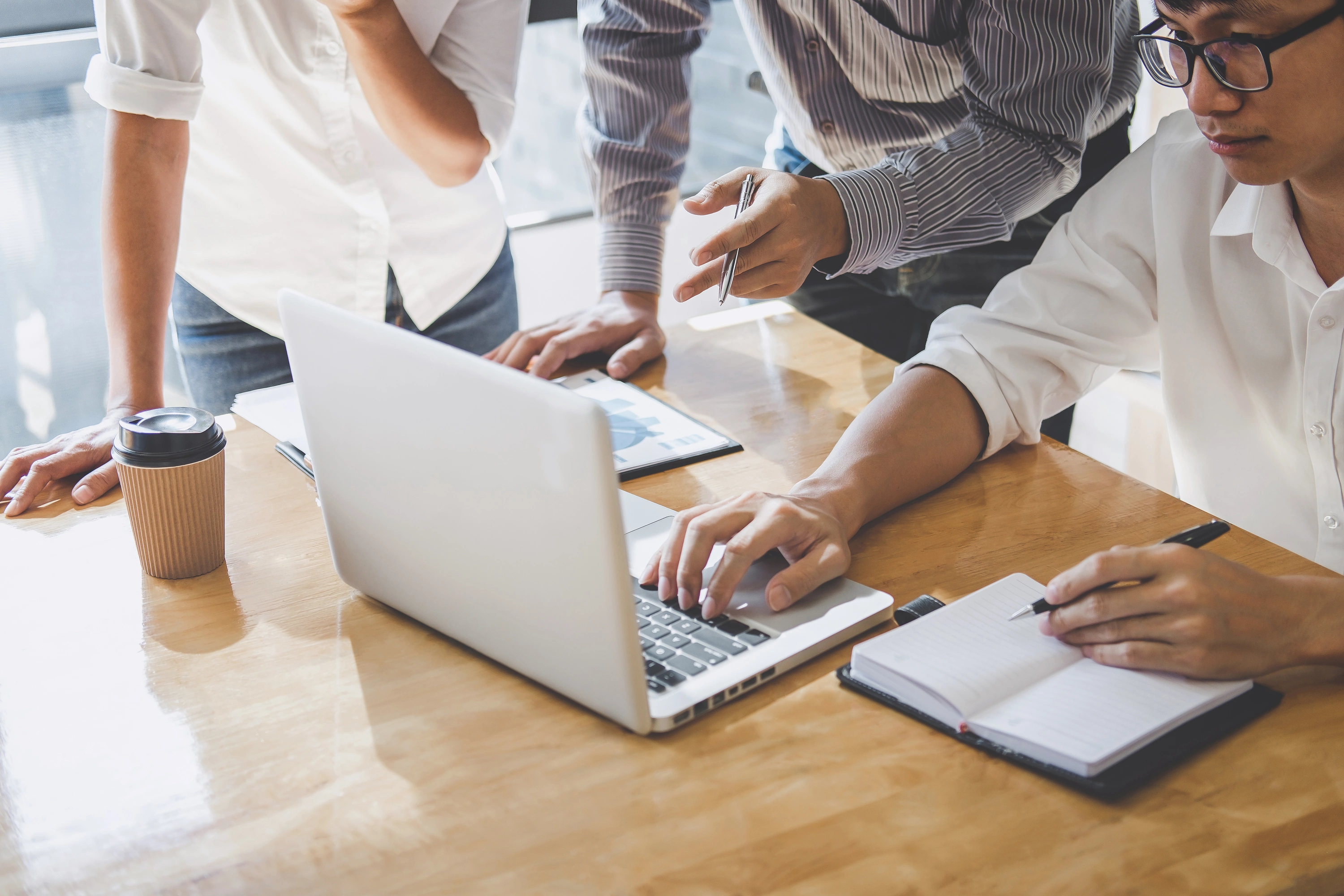 Mehrere Personen arbeiten gemeinsam an einem Holztisch mit Laptop und Dokumenten – Symbolbild für Teamarbeit oder Projektbesprechung.