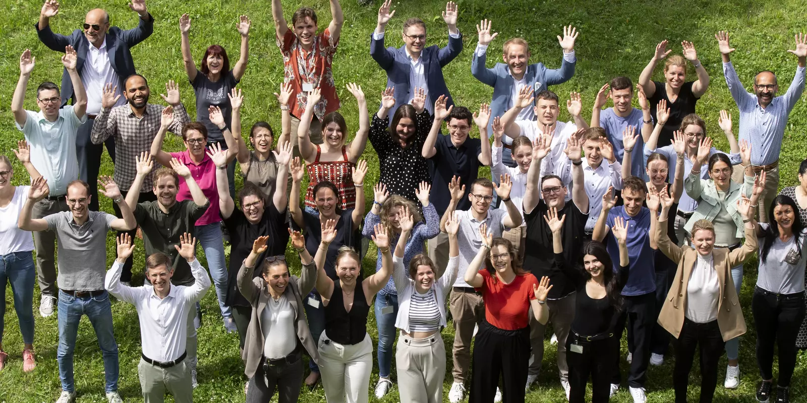 Gruppenfoto von Mitarbeitenden im Freien, die fröhlich in die Kamera winken.