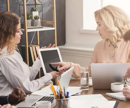 Gruppe von Geschäftsleuten bei einer Besprechung in einem modernen Büro, mit Laptops und Präsentationsmaterial.