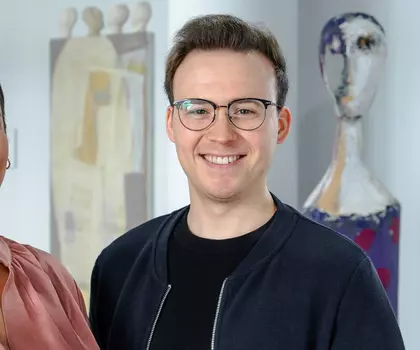 3 Personen stehen lächelnd nebeneinander in einem hellen Flur mit medizinischen Postern – Symbol für Team in einer medizinischen Einrichtung.