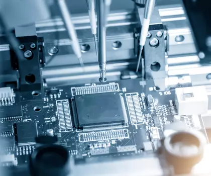 Nahaufnahme einer Leiterplatte mit elektronischen Bauteilen und präzisen Maschinenarmen – Symbolbild für Mikroelektronik.