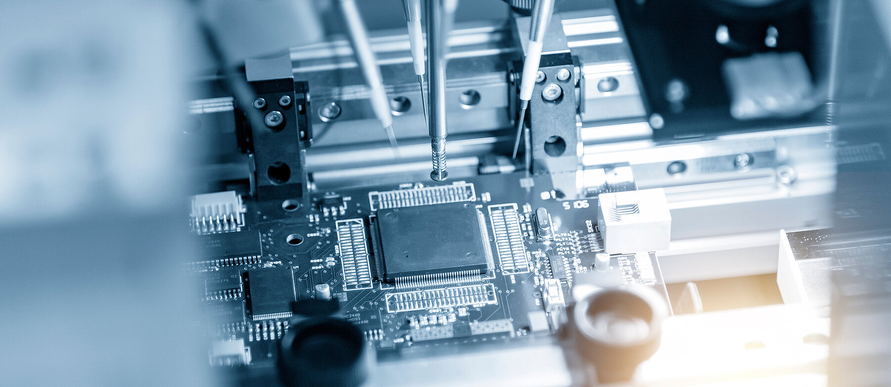 Nahaufnahme einer Leiterplatte mit elektronischen Bauteilen und präzisen Maschinenarmen – Symbolbild für Mikroelektronik.