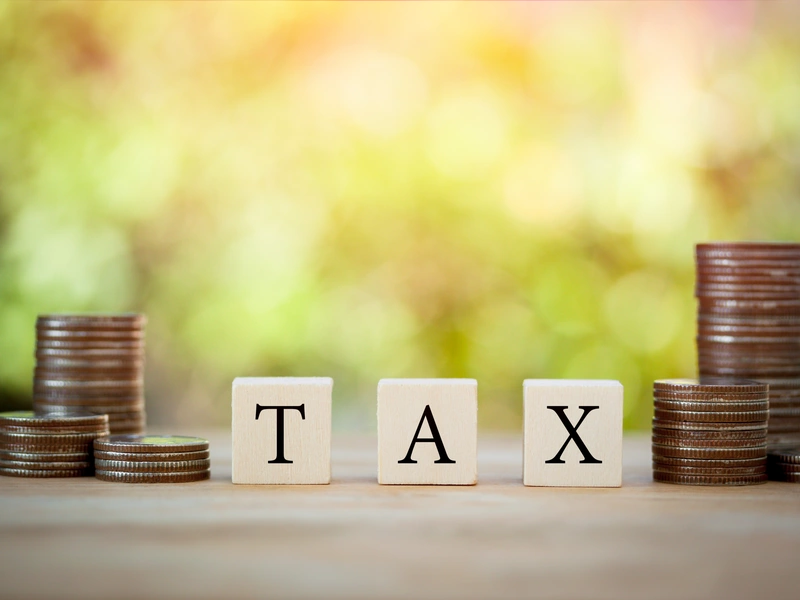 Bild von 3 Würfeln auf denen "Tax" steht, links und rechts jeweils ein Münzstapel