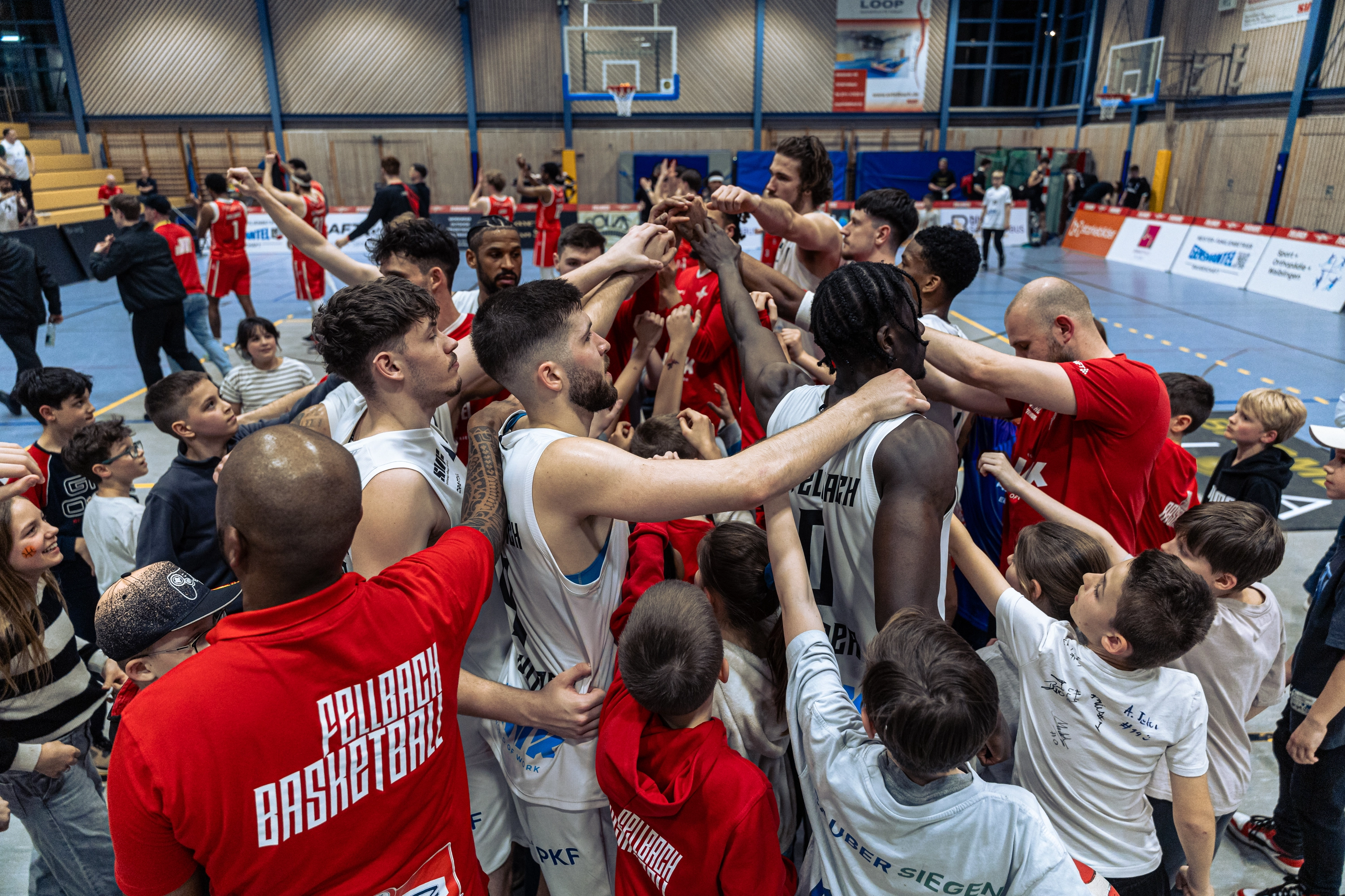 Basketballspieler und Fans feiern gemeinsam auf dem Spielfeld und strecken jubelnd die Hände in die Luft.