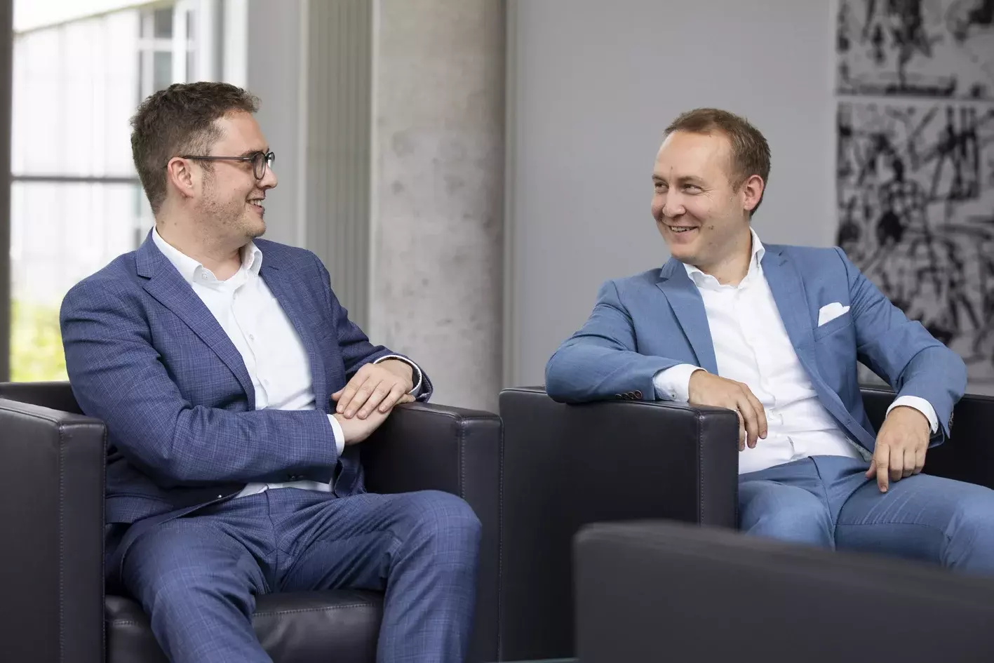 Zwei Männer in Businesskleidung sitzen entspannt in Sesseln und unterhalten sich – Symbolbild für Gespräch, Networking oder Geschäftsmeeting.
