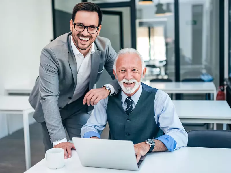 2 Geschäftsmänner an einem Schreibtisch, die an einem Laptop gemeinsam arbeiten