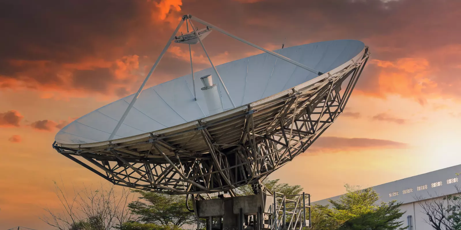 Große Satellitenschüssel vor einem farbenprächtigen Sonnenuntergang am Himmel.