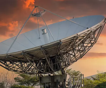 Große Satellitenschüssel vor einem farbenprächtigen Sonnenuntergang am Himmel.