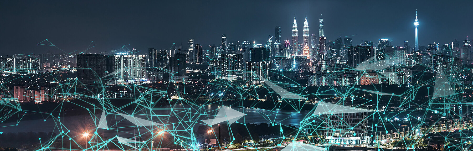 Nächtliche Stadtansicht mit leuchtender Skyline und überlagerten Netzwerklinien und Knotenpunkten – Symbol für Smart City.