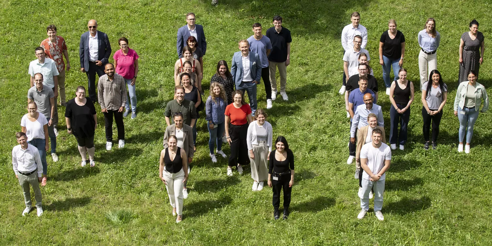 Gruppenfoto von Mitarbeitenden im Freien, die fröhlich in die Kamera winken.