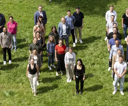 Gruppenfoto von Mitarbeitenden im Freien, die fröhlich in die Kamera winken.