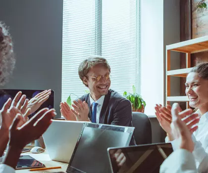 Gruppe von Geschäftsleuten in einem modernen Büro applaudiert gemeinsam während eines Meetings oder einer erfolgreichen Präsentation.