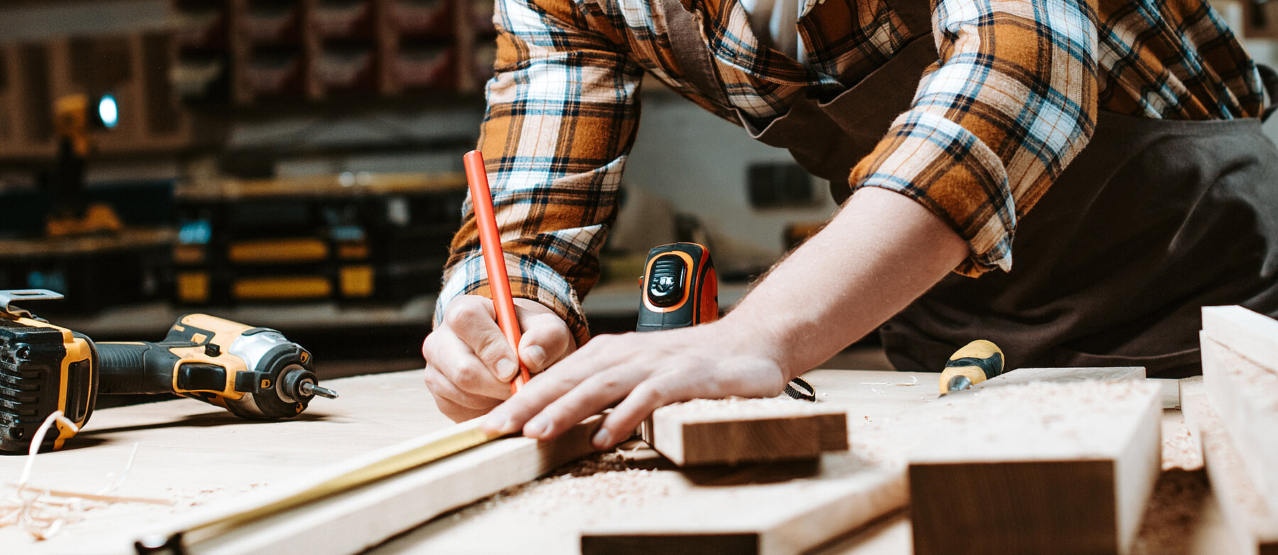 Handwerker misst und markiert Holz auf einer Werkbank, umgeben von Werkzeugen – Symbolbild für Tischlerei oder handwerkliche Präzisionsarbeit.