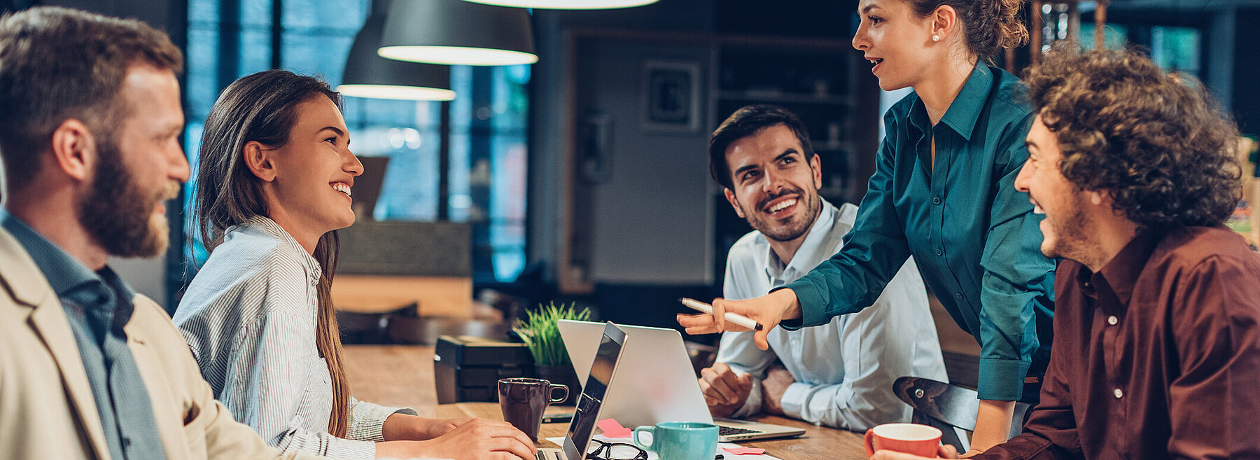 Gruppe junger Menschen in einem Büro sitzt um einen Tisch und diskutiert lebhaft – Symbolbild für Teamarbeit oder kreatives Brainstorming.