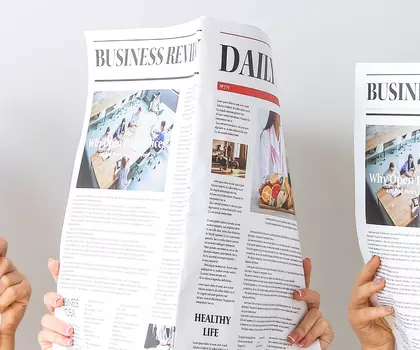 Mehrere Personen halten aufgeschlagene Wirtschaftsteil-Zeitungen vor sich, sodass nur die Zeitungen sichtbar sind.