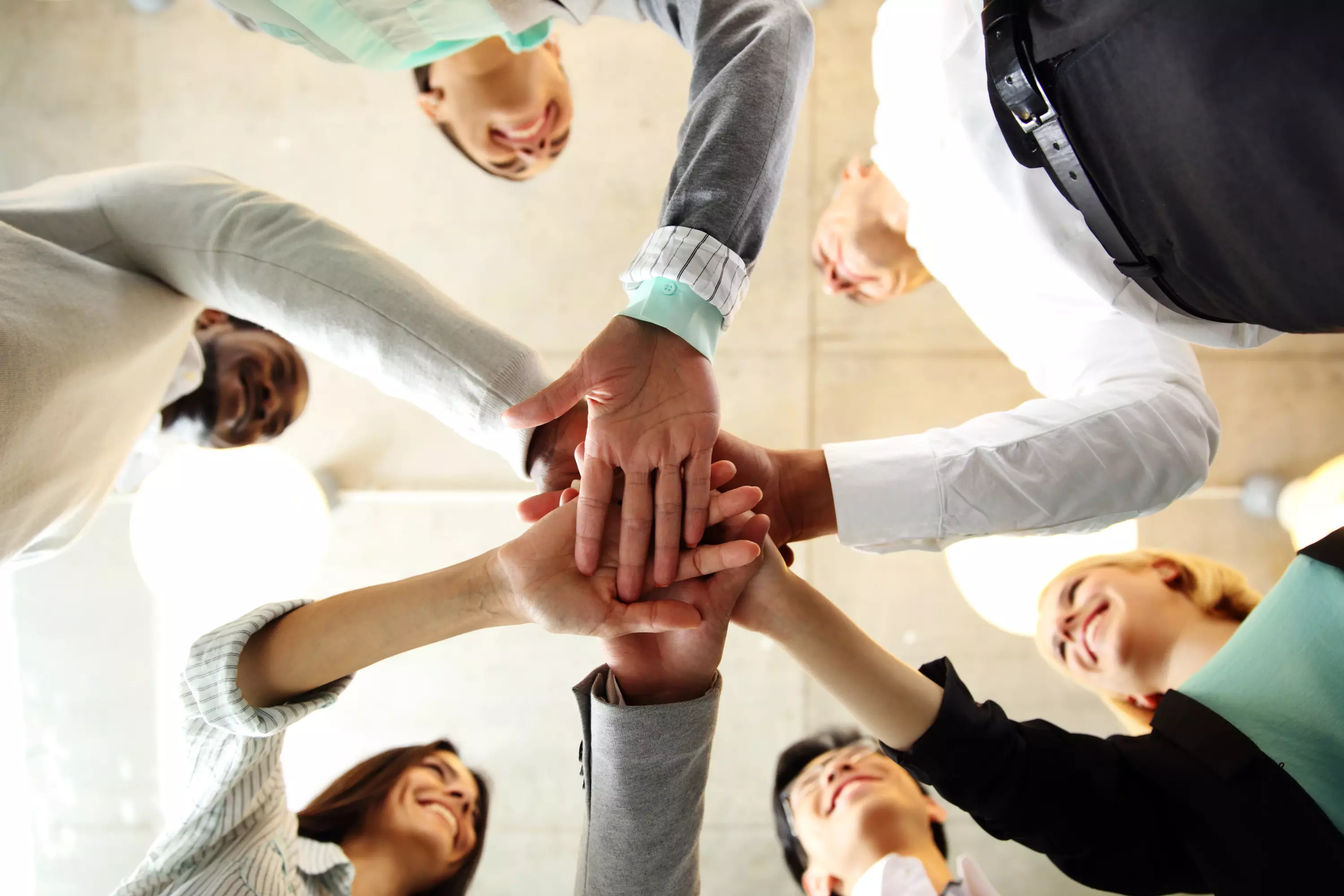 Gruppe von Menschen steht im Kreis und legt die Hände übereinander – Symbolbild für Teamwork, Zusammenhalt und Kooperation.