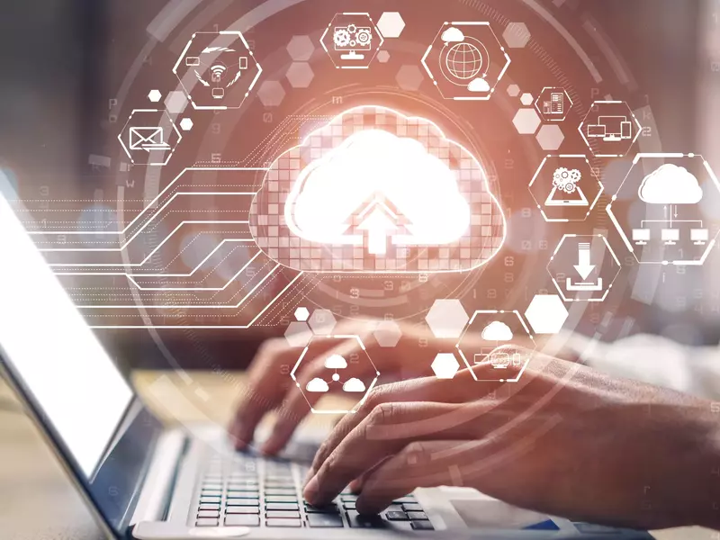 Bild von tippenden Händen an einem Laptop, darüber eine eingeblendete digitale Cloud