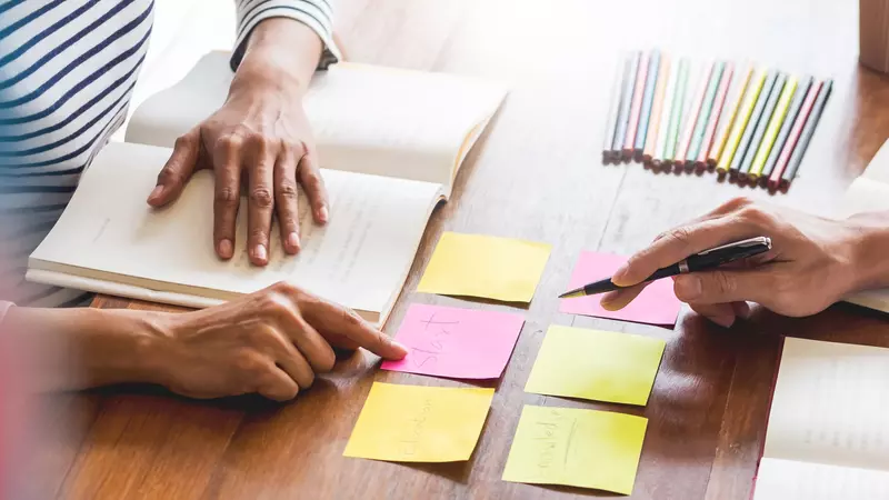 Bild von mehreren Personen, die gemeinsam an einem Tisch mit Notizbüchern, bunten Haftnotizen und einem kleinen Globus arbeiten