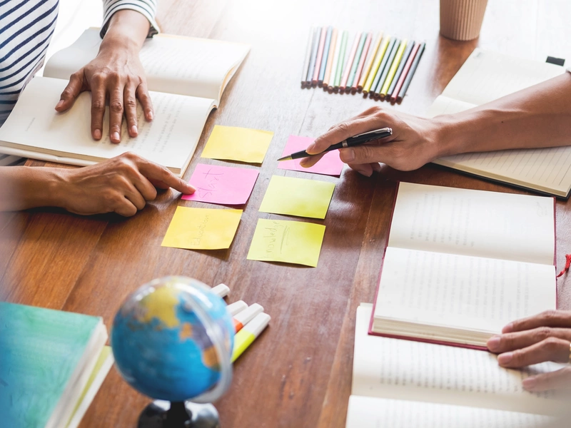 Bild von mehreren Personen, die gemeinsam an einem Tisch mit Notizbüchern, bunten Haftnotizen und einem kleinen Globus arbeiten