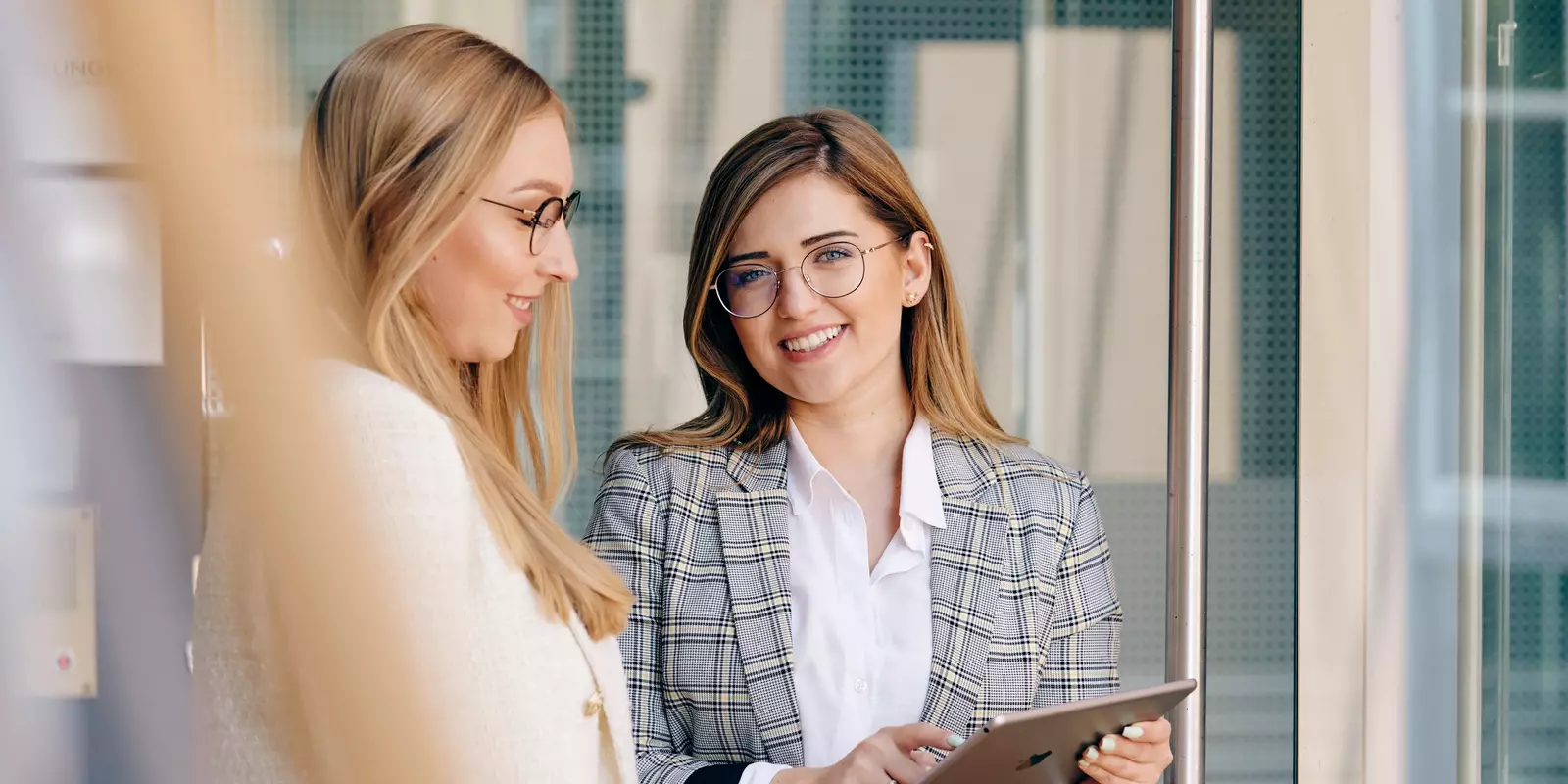 Zwei Geschäftsfrauen im Gespräch in einem Büro, eine von ihnen hält ein Tablet – Symbolbild für Zusammenarbeit oder Beratung im Business-Kontext.