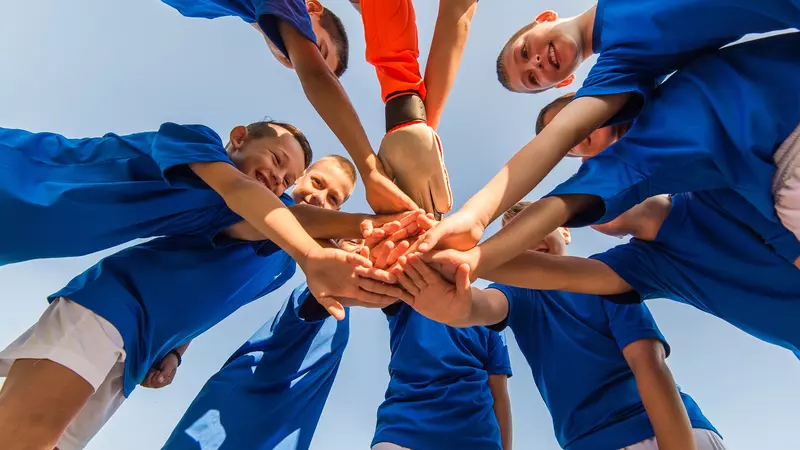 Bild einer Sportmannschaft, die in einem Kreis zur Motivation die Hände übereinander legt 