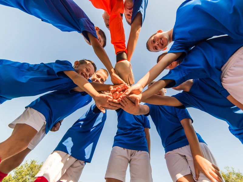 Bild einer Sportmannschaft, die in einem Kreis zur Motivation die Hände übereinander legt 