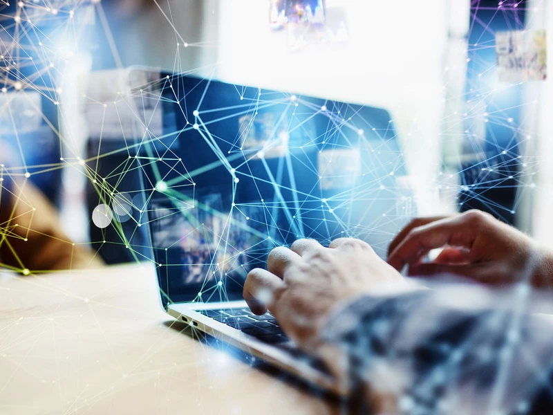 Bild einer Geschäftsperson, die an einem Laptop arbeitet, über ihr sind digitale Icons eingezeichnet, die Vernetzung symbolisieren