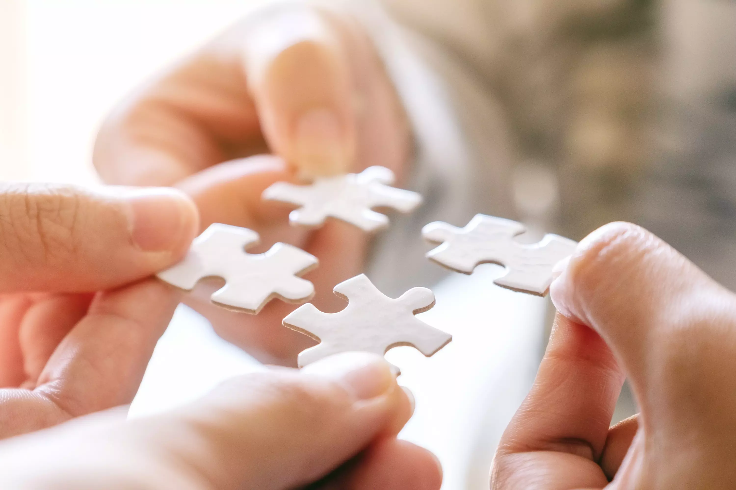 Zwei Hände fügen weiße Puzzleteile zusammen – Symbol für Zusammenarbeit.