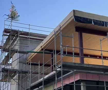 Neubau eines modernen Gebäudes mit Holz- und Glaselementen, eingerüstet für Bauarbeiten, unter blauem Himmel.