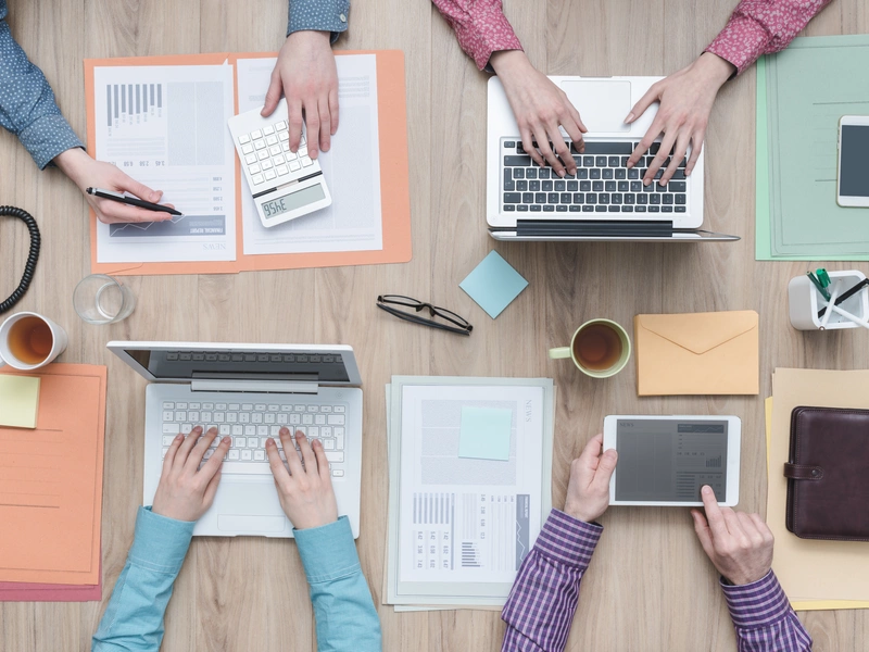 Bild von mehreren Personen, die gemeinsam an einem Tisch mit Notizbüchern und Laptops arbeiten