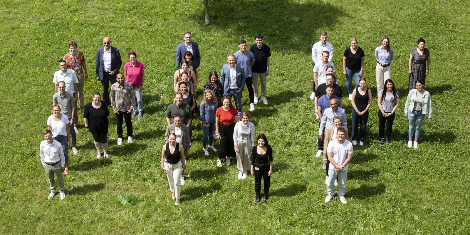 Bild aus der Vogelperspektive von Kollegen, die sich zusammen auf einer Wiese versammelt haben und Zusammenhalt zeigen