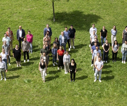Bild aus der Vogelperspektive von Kollegen, die sich zusammen auf einer Wiese versammelt haben und Zusammenhalt zeigen