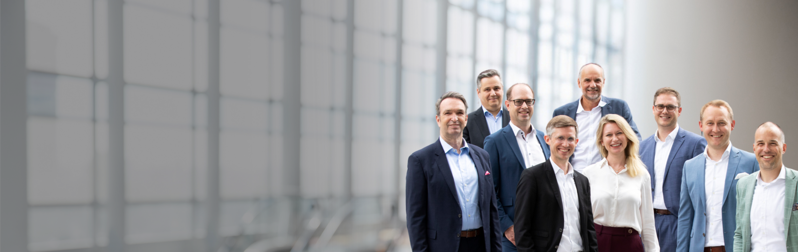 Geschäftsleute in Businesskleidung stehen vor einer modernen Glasfassade und blicken lächelnd in die Kamera – Symbolbild für Führungsteam.