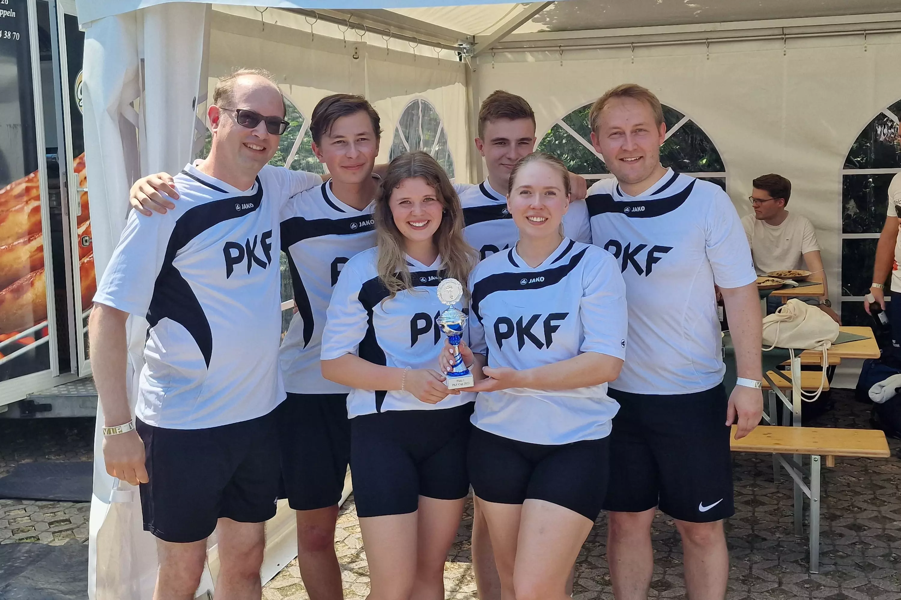 Gruppe von 6 Kollegen in einheitlichen Sporttrikots posiert vor einem Zelt – Symbolbild für Teamgeist und Firmenlauf.