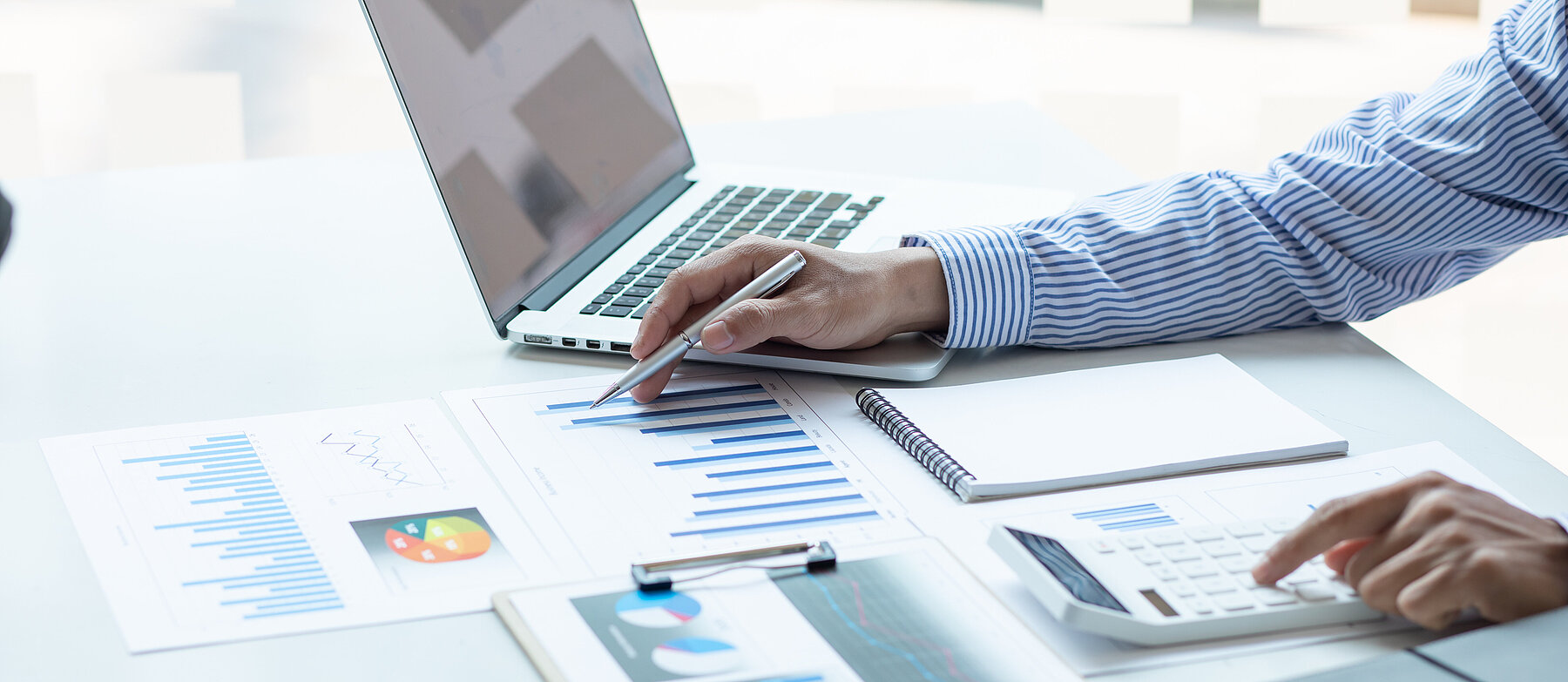 Person analysiert Diagramme und Finanzunterlagen am Schreibtisch mit Laptop, Tablet und Stift – Symbol für Datenanalyse oder Geschäftsplanung.