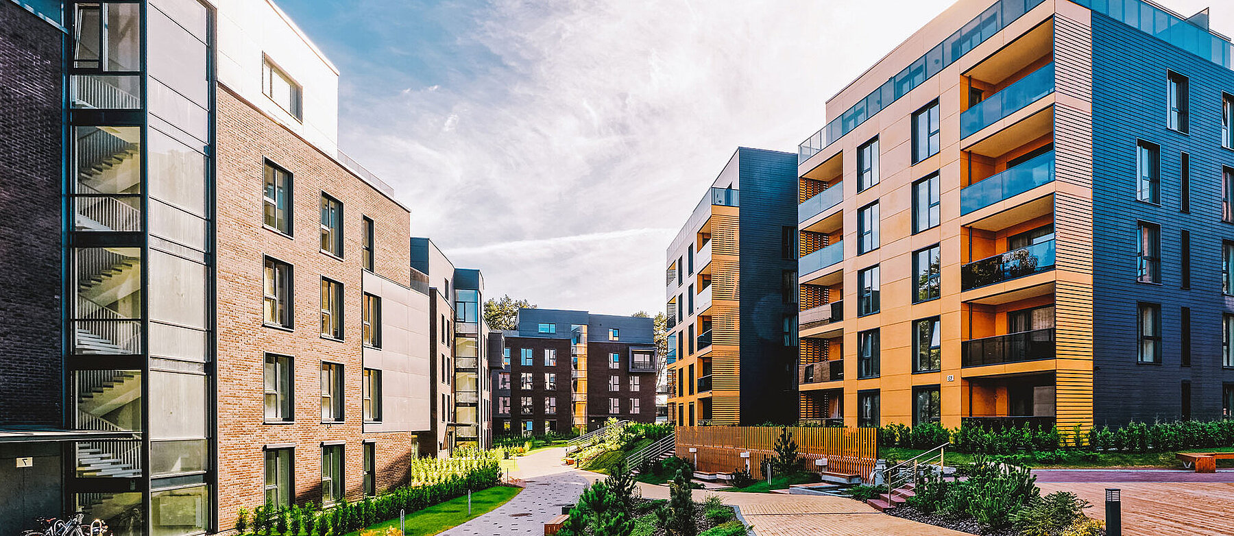 Moderne Wohnanlage mit mehrstöckigen Apartmentgebäuden, großen Fenstern und Balkonen, umgeben von gepflegten Grünflächen und Wegen.